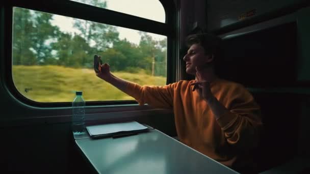 年轻人在旅行时坐火车 并通过智能手机的视频通话进行交流 盖伊打电话给车厢里的朋友们 — 图库视频影像