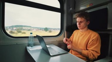 Yakışıklı genç adam kompartıman treninde masada oturuyor ve seyahat ederken dizüstü bilgisayarda film izliyor ve kablosuz kulaklıklardan gelen sesi dinliyor..