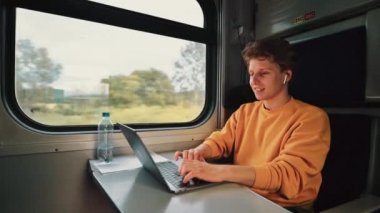 Yakışıklı genç adam trene biniyor ve dizüstü bilgisayarda çalışıyor. Yüzünde bir gülümseme var. Telsiz kulaklıkla iletişim kuruyor..