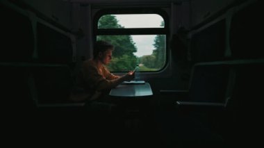 Genç bir adam akşam pencerenin yanında trene biner ve akıllı telefon kullanır. Tren konseptiyle seyahat.