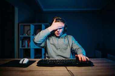 Kulaklık takan bir oyuncu, geceleri bilgisayarında mavi ışığı olan bir odada oturur ve avuç içi hareketi yapar. Oyun konsepti.