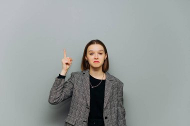 Gri arka planda izole edilmiş, üzgün kadın ofis çalışanı kameraya bakıyor ve boş alanda başparmaklarını gösteriyor. İş kadını duyguları fena değil. Gri arka planda izole edilmiş ceketli, üzgün kadın ofis çalışanı. Kameraya bakıyor ve seni gösteriyor.