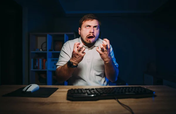 An emotional online worker gets angry while working at night on the computer. Angry programmer upset by a failure is emotionally angry.