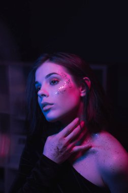 Parlak makyajlı çekici bir kadın. Yüzünde mor renkte pullar var. Mavi röfleli. Gece partisi. Neon