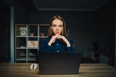 Güzel bir kadın, kablosuz kulaklıklı sadık bir işçi evde dizüstü bilgisayarın arkasında oturuyor ve ciddi bir yüzle kameraya bakıyor. Evde uzaktan çalışan serbest çalışan bir kadın..