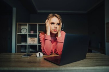 Yorgun kadın evinde, masasında dizüstü bilgisayarıyla oturmuş üzgün bir suratla yüzünü çeviriyor..