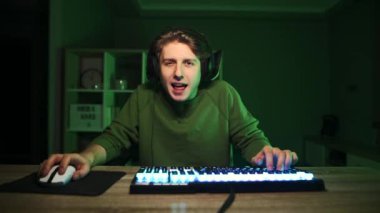 Neşeli adam yeşil ışıkta bilgisayarda oyun oynuyor ve yüzünde bir gülümsemeyle iyi bir hareket sergiliyor..