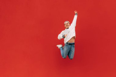 Neşeli öğrenci elinde dizüstü bilgisayarla kırmızı bir duvarın arka planında zıplıyor, kameraya bakıyor ve gülümsüyor..