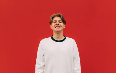 Beyaz kazaklı olumlu bir adam kırmızı arka planda akıllı telefon kullanıyor ve gülümsüyor. Boşluğu kopyala