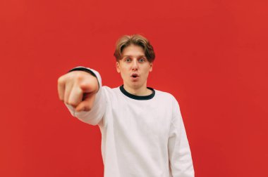 Ağzı açık neşeli bir adam kameraya bakar ve arka plandaki kırmızı duvarı işaret eder..