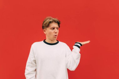 Şaşırmış adam elinde fotokopi alanını tutuyor ve ağzı açık bir şekilde kırmızı bir duvarın arka planına bakıyor..