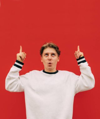 Kırmızı duvarda beyaz giysili, şaşkın bir adam var. Arka planda ve fotokopi uzayında parmakla görünüyor. Dikey