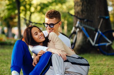 Birbirlerine bakıp, eğlenen, şehir parkında dikkatsiz hisseden neşeli bir çiftin portresi. Erkek ve kadın, dişlek gülümsemelerle kucaklaşıp gülümsüyor..