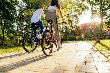 İki arkadaş, bir erkek ve bir kadın, modern renkli bisikletleriyle dışarıda yarışıyorlar. Çift spor kıyafetleri giyiyor, arka planda güneş ışığı, arka plan.