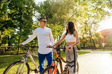 Erkek arkadaşı ve kız arkadaşı bisikletleriyle parkta yürürken birbirlerine tutkuyla bakıyorlar. Çiftler şık günlük kıyafetler giyerler..