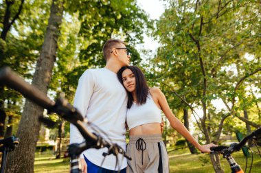 Romantik, hassas, genç bisikletçi çift şehir parkında duruyor, sarılıyor, bisikletlerini tutuyor, rahat ve sakin hissediyorlar..