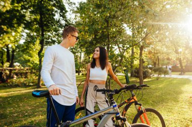 Fotojenik gülümseyen birkaç motosikletli parkta yeşil çimlerin üzerinde durmuş sohbet ediyor, birbirlerine bakıyor, birlikte vakit geçiriyorlar..