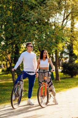 Şehir parkındaki güneş ışığına bakan bisikletçilerin dikey çekimleri, arka plandaki güzel doğa..