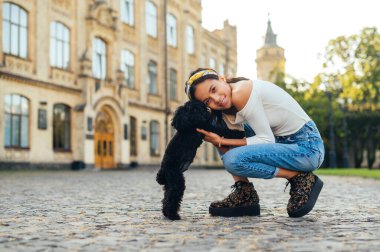 Kasabanın arka planında küçük sevimli bir köpekle gülümseyen kadının portresi. Tarihi mimari, sarılma ve mutlu yüzle kameraya bakma..