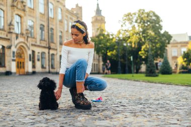 Güzel bir manzaranın arka planında parktaki kaldırım taşlarının üzerinde tatlı siyah bir köpekle oynayan bir kaniş oyuncağı..