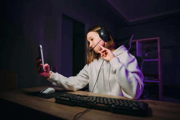 美しい女性のスリマーは ヘッドセットのコンピュータで夜に座って スマートフォンのカメラで加入者と通信し オンラインゲームをプレイ — ストック写真