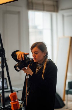 Bir fotoğraf stüdyosunda elinde kamerayla duran ve ekrana bakan kamerayı ayarlayan profesyonel bir kadın fotoğrafçının portresi. Dikey