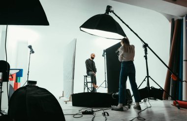 Sahne arkası fotoğrafı, kadın fotoğrafçı ve erkek model beyaz arka planda çalışıyor.