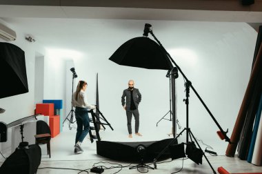 Sahne arkası fotoğrafı, kadın fotoğrafçı ve erkek model beyaz arka planda çalışıyor.