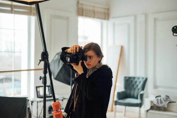 Female photographer in the studio at work, makes a photo shoot with a serious face.