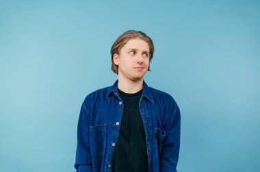 Tişörtlü komik bir adam mavi arka planda duruyor ve başka yere bakıyor. Mavi gömlekli, komik bir yüzü var..