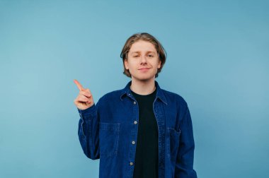 Mavi tişörtlü pozitif bir adam dünya duvarının arka planında izole edilmiş. Yüzünde bir gülümsemeyle kameraya bakıyor ve parmağını yan tarafa doğrultuyor..