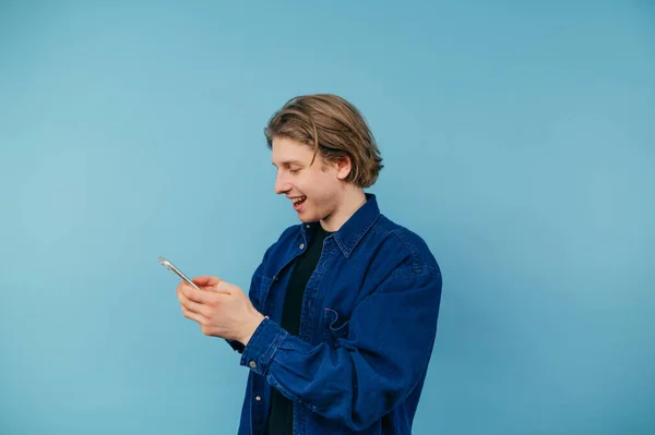 Positive Guy Blue Shirt Stands Colored Background Communicates Smartphone Smile — Foto Stock