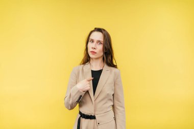 Şaşırmış bej takım elbiseli kadın ofis çalışanı kameraya bakar ve sarı arka planda izole edilmiş şok olmuş bir yüzle kendini gösterir..