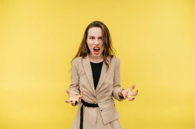 Kızgın ve bağıran takım elbiseli saldırgan bir kadın işçinin portresi, kameraya ağzı açık, sarı bir arka planda izole bir şekilde bakıyor..