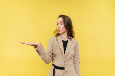 Bej takım elbiseli sevimli bayan işçi elinde fotokopi alanı tutuyor ve sarı arka planda şaşırmış bir yüzle başka yere bakıyor..