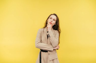 Sarı arka planda bej takım elbiseli düşünceli bir kadının portresi, ciddi bir yüz ifadesiyle başka yere bakıyor ve düşünüyor..