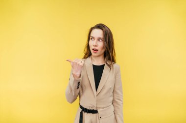 Bej takım elbiseli şaşırmış bir kadın parmağını fotokopi odasında gösteriyor ve sarı arka planda izole edilmiş, şok olmuş bir yüzle bakıyor..