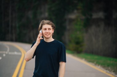 Hafta sonu parkta yürürken olumlu adam bir dağ yolunda dikiliyor kozalaklı ağaçların arka planında ve yüzünde bir gülümsemeyle başka yere bakıyor..