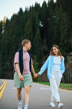Ormanda bir dağ yolunda el ele tutuşan mutlu turistler sevdiklerine bakıp gülümsüyorlar. Dikey