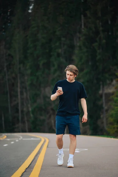 Jovem Bonito Caminha Uma Estrada Asfalto Montanha Contra Pano Fundo — Fotografia de Stock