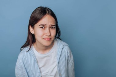 Young woman with a confused expression against a blue background.