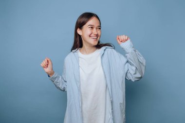 Smiling woman in casual attire dancing against a blue background.