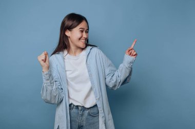 Young woman smiling and pointing sideways against blue background.