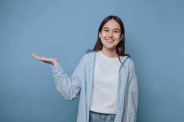 Smiling young woman presenting with open hand against blue background.