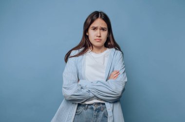 Young woman with crossed arms looking displeased against blue background.