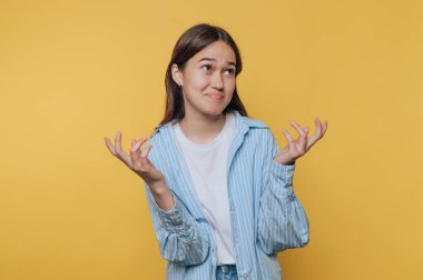 Young woman shrugging with a confused expression against a yellow background.
