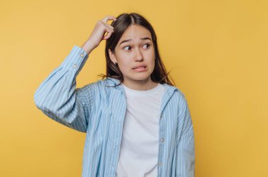 A young woman looking confused, scratching her head, with a worried expression, against a bright yellow background