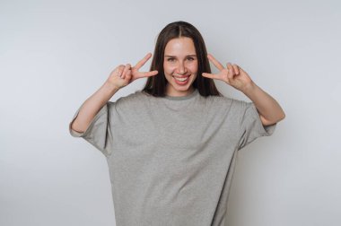 Smiling woman in gray shirt making peace signs with both hands.