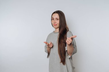 Young woman with long hair in casual gray shirt pointing fingers.
