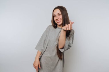 Smiling woman in gray t-shirt making a heart gesture with fingers.